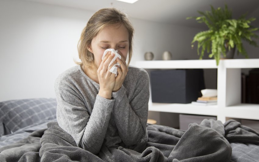 sick woman sitting bed blowing nose with napkin 